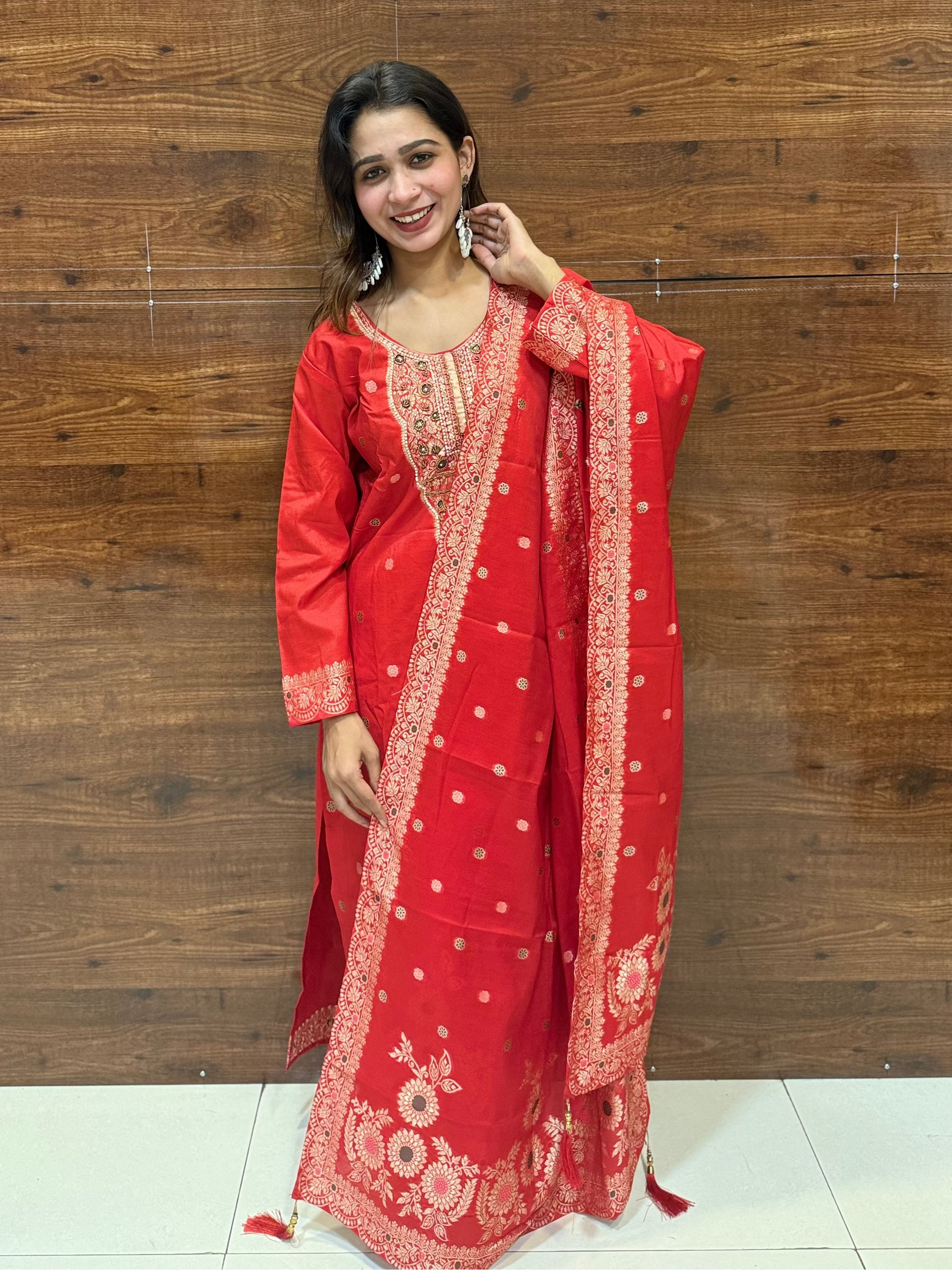 Woman in a red traditional outfit standing against a wooden wall.